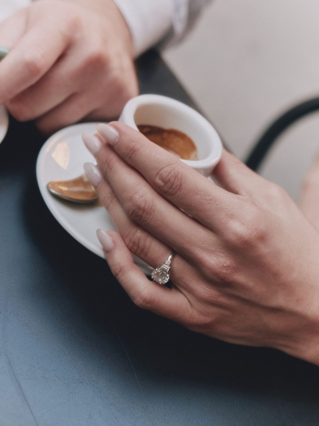 Her hand with the engagement ring holding an espresso